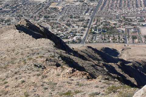 A rocky desert ridge falling away toward a grid of houses and streets and a white temple with spires