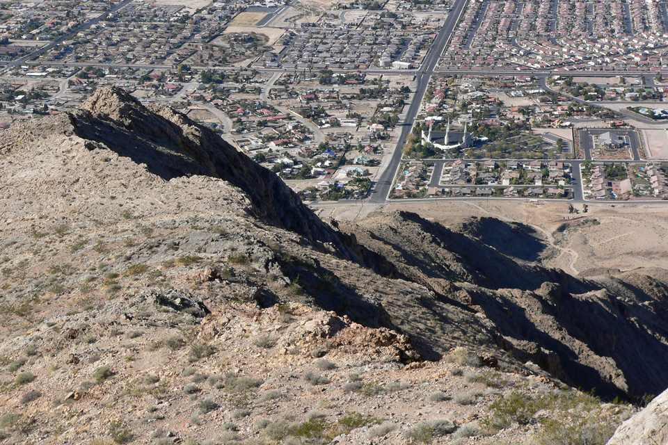 A rocky desert ridge falling away toward a grid of houses and streets and a white temple with spires
